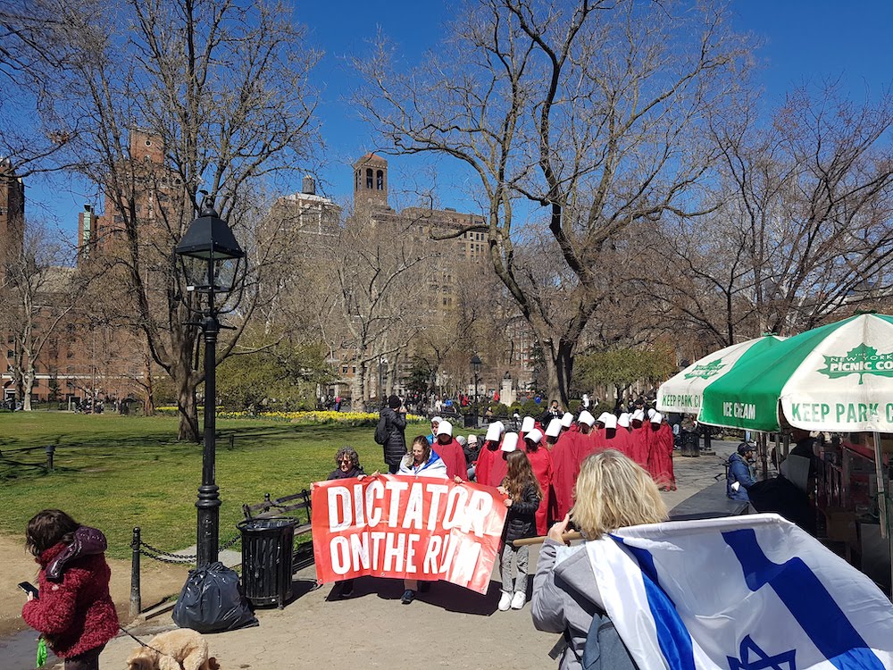 Handmaid protest in Washington Park. They are carrying a sign that reads "Dictator on the run"